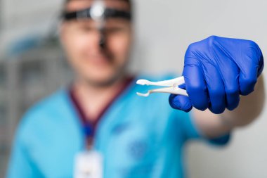 Diş hekimi rutin bir diş muayenesi sırasında diş çekmek için hazırlanıyor. Önlüklü bir diş hekimi, ameliyatta kullanılan diş aletini göstermek için dişini çıkarmaya hazır..