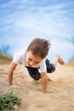 Güneşli bir günde göl kenarında kumlu bir tepede sürünen bir çocuk. Genç bir çocuk kumlu bir yamaçta sürünmekten zevk alıyor. Parlak bir gökyüzünün altında gölün kenarında gülüyor ve oynuyor..