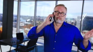 Mavi gömlek giyen rahat olgun bir adam ofiste telefonda konuşuyor. Adam konuşmayı bitirir ve telefonunu öper..