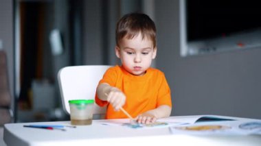 Sevimli erkek bebek sanata odaklanmış. Çocuk boyama kitabı için fırça kullanıyor. Bulanık arkaplan.