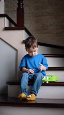 Evdeki merdivenlerde oturan Kafkasyalı çocuk. Küçük çocuk güneş gözlüğünü çıkarıp ayağa kalkar ve uzaklaşır. Dikey video.