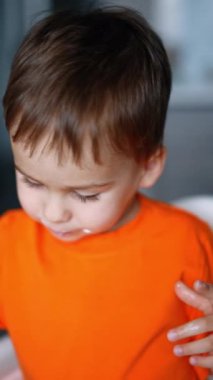 Beyaz bıyıklı, tatlı, beyaz bir bebek. Yoğurt yiyip tezahürat yapan sevimli çocuk. Kapatın. Dikey video.