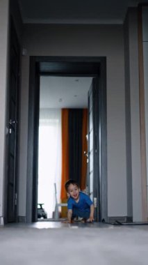 Neşeli beyaz bir erkek bebek yere yığıldı. Çocuk evde neşeyle oynuyor. Dikey video.