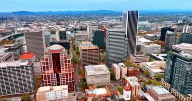 Portland şehir merkezinde çok katlı binaların çeşitliliği. Willamette Nehri metropolü geçer. Dağlardaki siluetler arka planda.