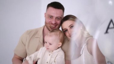 Ellerinde sevgili bir bebekle genç, beyaz bir aile. Mutlu anne ve babalar ve oğulları stüdyoda. Beyaz arkaplan.