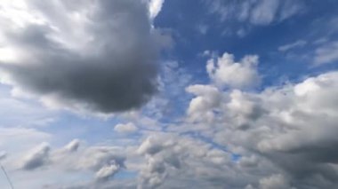 Mavi gökyüzünde süzülen bulutların arasında uçuyor. Kabarık gri bulutlar atmosferde şekil değiştiriyor. Zaman Uygulaması.