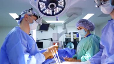 Bir grup sıhhiyeci ameliyathanede hastanın yanında duruyor. Başhekim hemşirenin aletlerini alıp beyin cerrahisinde kullanıma hazırlıyor..