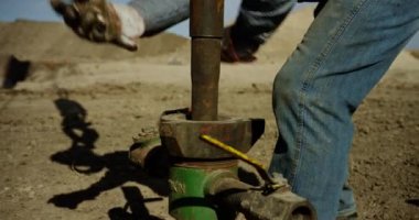 Kirli kot giyen tanınmamış işçi borudaki metal elementi döndürüyor. Petrol veya gaz üretimi için ekipman düzenleniyor.