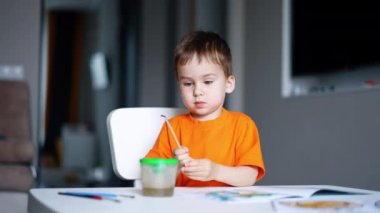 Masada oturan şirin beyaz bebek elinde boya fırçası tutuyor. Bebek fırçayı koyar ve masadan kalkar. Bulanık arkaplan.