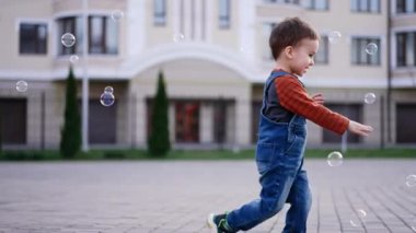 Mutlu gülümseyen bebek sabun köpüklerini yakalıyor. Enerjik çocuk dışarıda eğleniyor..