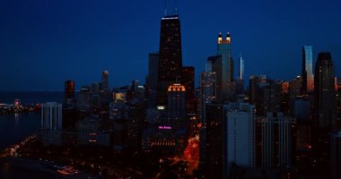 Şehir merkezindeki pencerelerde çeşitli binalar ve ışıklar görünüyor. Şikago, Illinois, Amerika Birleşik Devletleri 'nin alacakaranlıkta panoramasından yükseliyor..