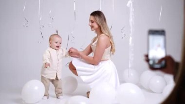 Mutlu anne bebeğini elinden tutuyor. Güzel gülümseyen çocuk yürümeyi öğreniyor. Stüdyo görüntüleri.