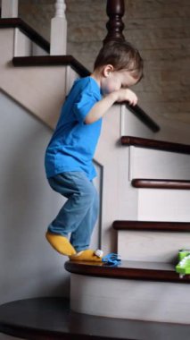 Sevimli erkek bebek, güneş gözlüğü ve gitarın olduğu merdivenlere dikkatle basıyor. Çocuk ellerini sallıyor. Dikey video.