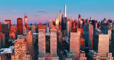 Günbatımının ışığı New York manzarasında birden fazla binanın cephelerini yansıtıyor. Metropolü kaplayan pembe gün batımı ışığı. Üst görünüm.