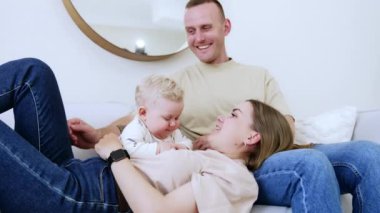 Kafkasyalı mutlu ebeveynler bebekleriyle birlikte dinleniyorlar. Küçük çocuk annesinin yanında kocasının kucağında yatıyor. Gururlu baba oğlunun başını okşar..