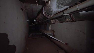 Bodrumun tavanında çeşitli genişlikte metal borular var. Işıksız eski bir binanın karanlık önermesi.