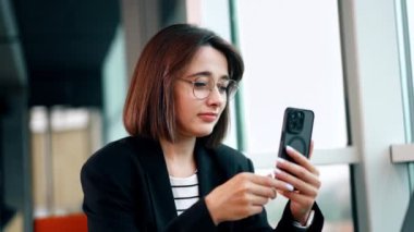 Gözlüklü güzel esmer dizüstü bilgisayarın önünde oturuyor. Bayan selfie çekmek için akıllı telefonunu kullanıyor..