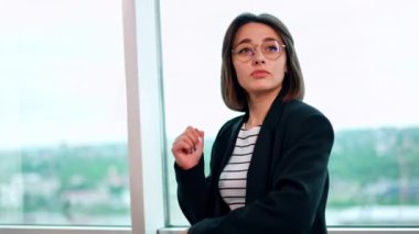 Genç pozitif beyaz tenli, gözlüklü esmer pencerede dans ediyor. Kadın ceketini çıkardı ve sıcak bastı..