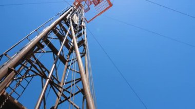 Long metal pipe attached to the wire is wobbling from side to side. A tower for drilling oil and gas beside. Low angle view.