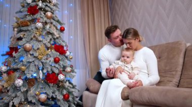 Üç kişilik mutlu bir aile Noel tatilini evde kutluyor. Anne bebeğini başından öperken, adam karısını öpüyor..