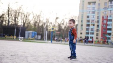 Dışarıda sabun köpüklerini yakalayan sevimli mutlu çocuk. Yürüyüşteki neşeli, aktif bir çocuğun portresi.