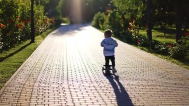 Motosiklete binen bir bebeğin arka görüntüsü. Üç yaşındaki küçük çocuk çizgili gömleğiyle güzel parkın yanından neşeyle geçiyor..
