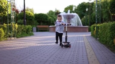 Enerjik beyaz çocuk scooterını çekerek koşuyor. Aktif üç yaşında bir çocuk yazın parkta eğleniyor..