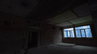 Büyük pencereli büyük odada çıplak tuğla duvarlar. Tavanda kalın tel ve ampul asılı. İnşaat veya yeniden yapılanma süreci.