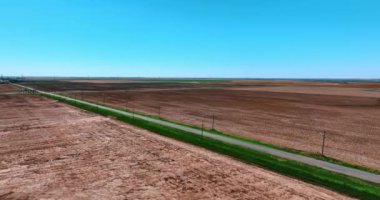 Yeşil çimlerle kaplı asfalt yol uçsuz bucaksız araziyi geçiyor. Issız toprakların üstündeki drone görüntüleri..