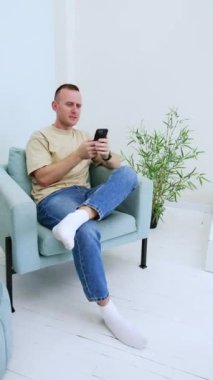Mutlu gülümseyen adam elinde telefonuyla sandalyede oturuyor. Alet kullanmaya başlayınca insanın morali bozuluyor. Dikey video.