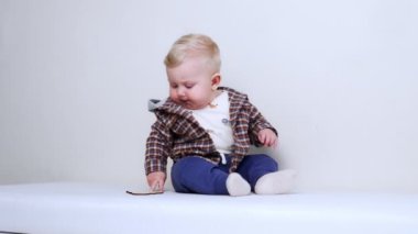 Kareli ceketli güzel sarışın erkek bebek yerde oturuyor. Ciddi çocuk tahta tabelayla oynuyor. Dikey video.