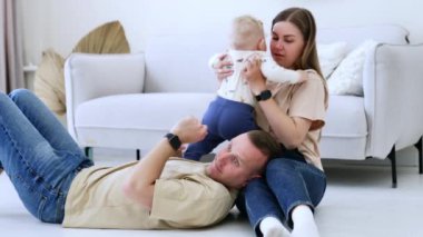 Üç kişilik aile evde birlikte vakit geçiriyor. Babam annemin dizlerinin üstüne çöker ve bebek babamın yüzüne bakar..
