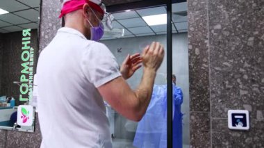 Erkek doktor elini sensörün yakınına koyup modern operasyon odasının kapısını açıyor. Bir hemşire onun için hazırlanmış bornozlu cerrahı bekliyor. Sağlık personeli, cerrahın ceketi giymesine yardım eder..