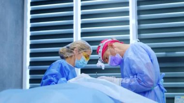 Hastanın başında duran doktor metal aletleri dikkatlice kullanır. Kadın hemşire tiroid göz ameliyatında cerraha yardım etmek için yakın duruyor..