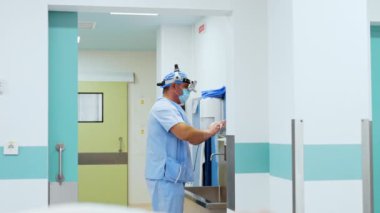 Açık mavi üniformalı, şapkalı, maskeli ve cerrahi aletli bir cerrah ellerini dikkatlice yıkar. Ameliyattan önce hastanede temizlik işleri vardı..