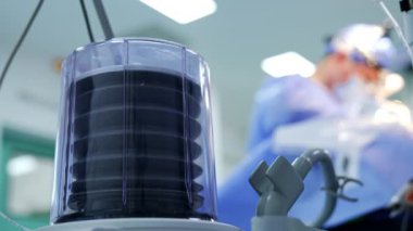 Ameliyat altındaki hastaya hava pompalayan akciğer solunum cihazı. Düşük açılı görüş açısını kapat. Arkaplanda ameliyat yapan doktorun bulanık görüntüsü.