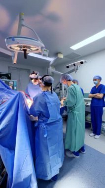 Profesyonel cerrahlar operasyon masasının etrafında dururlar. Diğer tıbbi personel ameliyathanedeki çeşitli ekipmanlarda çalışıyor. Dikey video.