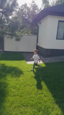 Bahçedeki yeşil çimlerin yanından koşan sevimli bir erkek bebek. Aktif çocuk yazın dışarıda eğleniyor. Dikey video.