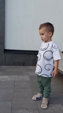 Bahçede yeşil çimlerle koşan sevimli erkek bebek. Neşeli mutlu çocuk dışarıda eğleniyor. Dikey video.