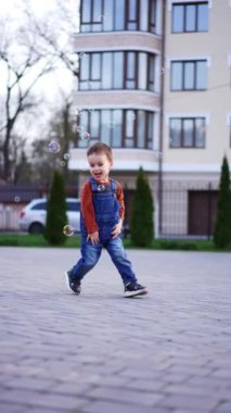 Güzel bebek uçan sabun köpüklerini yakalıyor. Sevimli mutlu çocuk neşeyle koşuyor. Düşük açı. Dikey video.