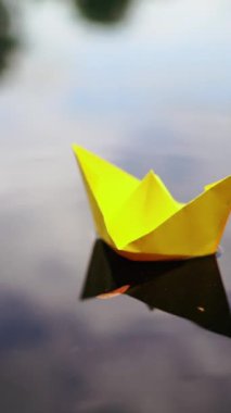 Kağıt gemi kadının elinde. Kadın tekneyi suya batırıyor. Dikey video