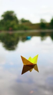 Mavi su yüzeyinde yüzen kağıt tekne. Mavi temiz nehirde sessizce yüzen basit bir origami kağıt tekne. Dikey video