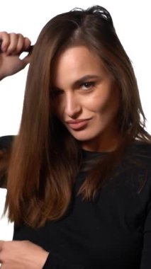 Saçlarını tarayan zavallı kadın. Beyaz arka planda, saçlarını tarayan, dokunaklı bakışları olan, oldukça çekici bir kadın. Dikey video