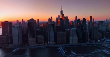 Gün batımında Manhattan 'ın silüeti. Arka planda göz kamaştırıcı pembe gökyüzü. İnsansız hava aracı görüntüsü şehirden uzaklaşıyor.