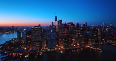 Alacakaranlıkta Manhattan 'ın parlak silueti. Doğu Nehri 'nin yukarısından insansız hava aracı görüntüleri. Arkaplanda pembe gökyüzü.