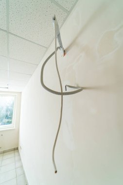 Ofisteki bir duvarda asılı elektrik kablosu. Bir elektrik teli tavandan boş bir ofis alanına sarkıyor ve pencereden içeri doğal ışık giriyor..
