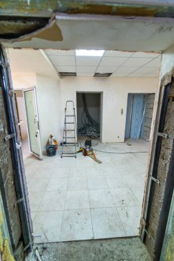 Bitmemiş bir odada malzemelerle yenileme işlemi devam ediyor. Tamamlanmış bir alanın aksine, bu tamamlanmamış oda yenileme sırasında araçları, enkazı ve inşaat malzemelerini sergiler.