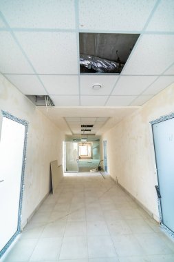 Açık tavanlı uzun bir koridor tadilatta. Açık tavan ve enkazlarla dolu bitmemiş bir koridor, devam eden yenileme çalışmalarını gösteriyor..