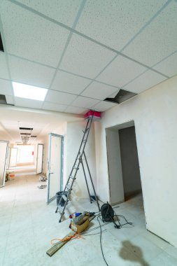 Merdiven ve tavan tamiri olan bir ofis alanında tadilat işi. Tadilat yapılan bir ofiste, tamirat için tavan panelleri çıkarılan ve zemine saçılmış aletler olan bir merdiven var..