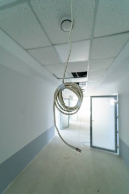 Öğlen vakti tavanı açık, bitmemiş bir koridorda asılı bir kablo. Açığa çıkmış ışıkları ve tamamlanmamış duvarları olan boş bir koridorda asılı bir kablo var.